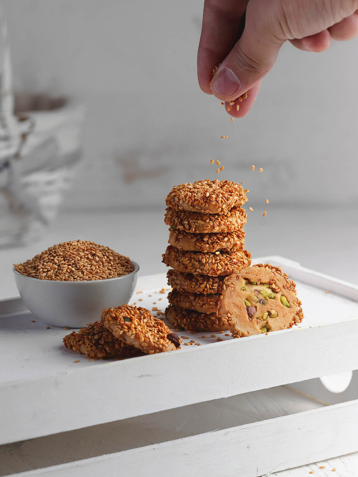 A hand sprinkling white sesame on top of sesame cookies.