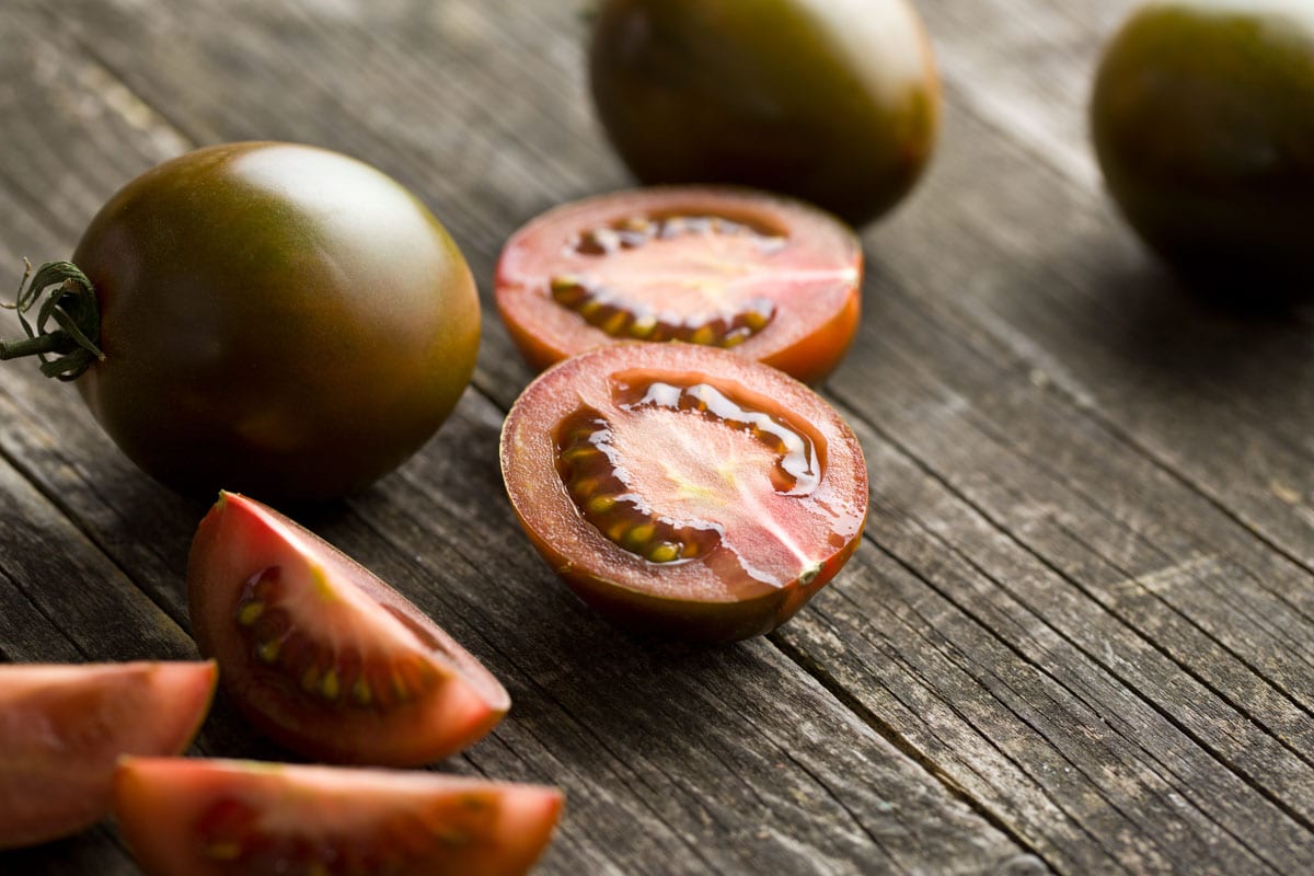 Halved dark tomatoes on old wooden table.