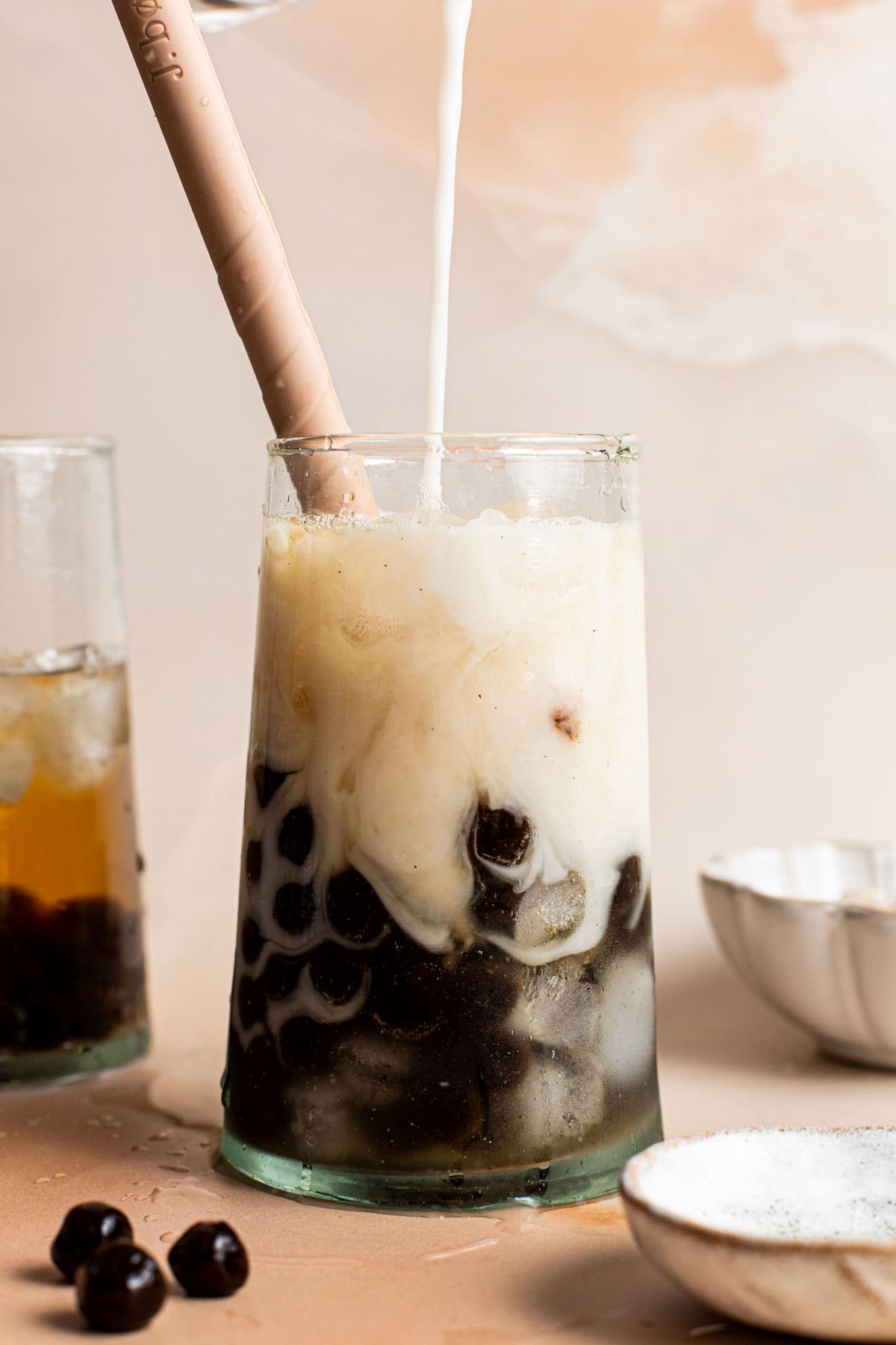 Milk being poured into a glass filled with ice, tapioca pearls and tea. 