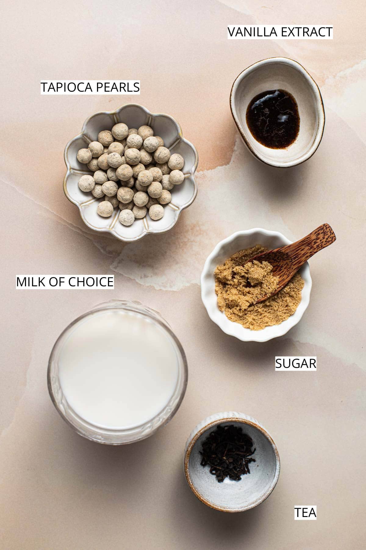 Vanilla, sugar, tea, milk and tapioca pearls on a flat surface.