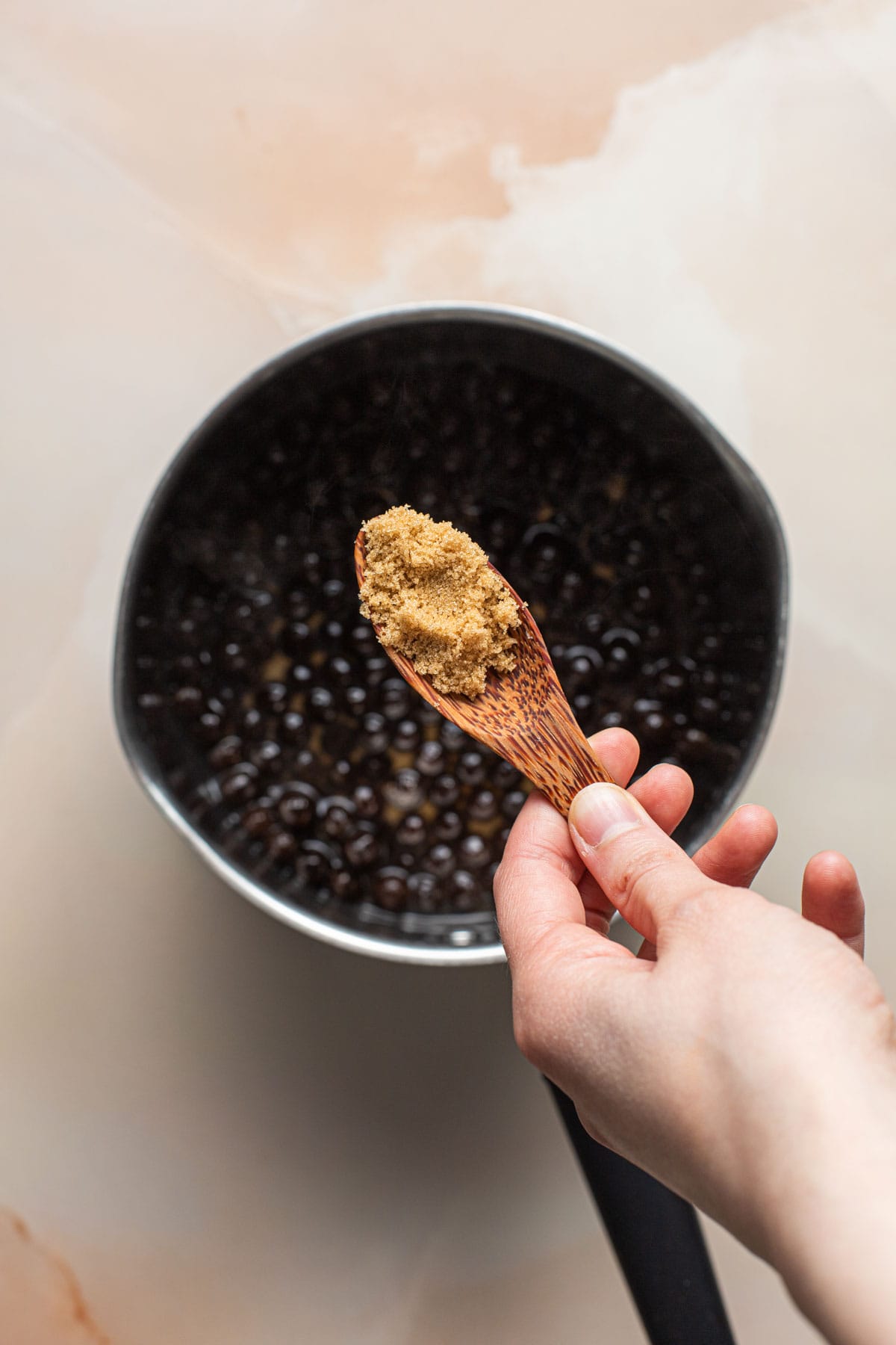 A hand holding out brown sugar above a pan of tapioca pearls.