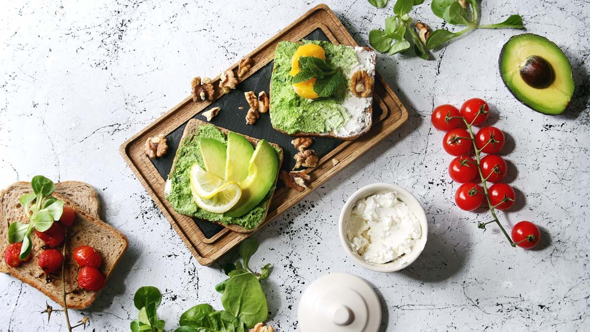 Vegetarian sandwiches with avocado, ricotta, egg yolk, spinach, cherry tomatoes on whole grain toast bread.