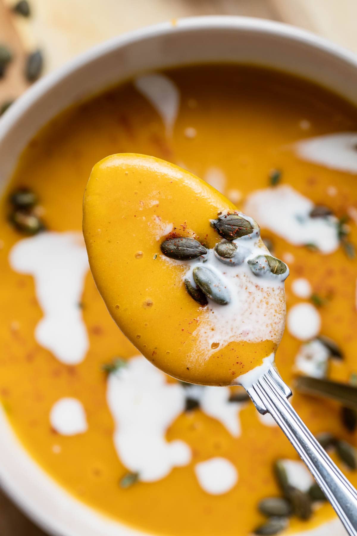 A spoon filled with soup and pumpkin seeds. 