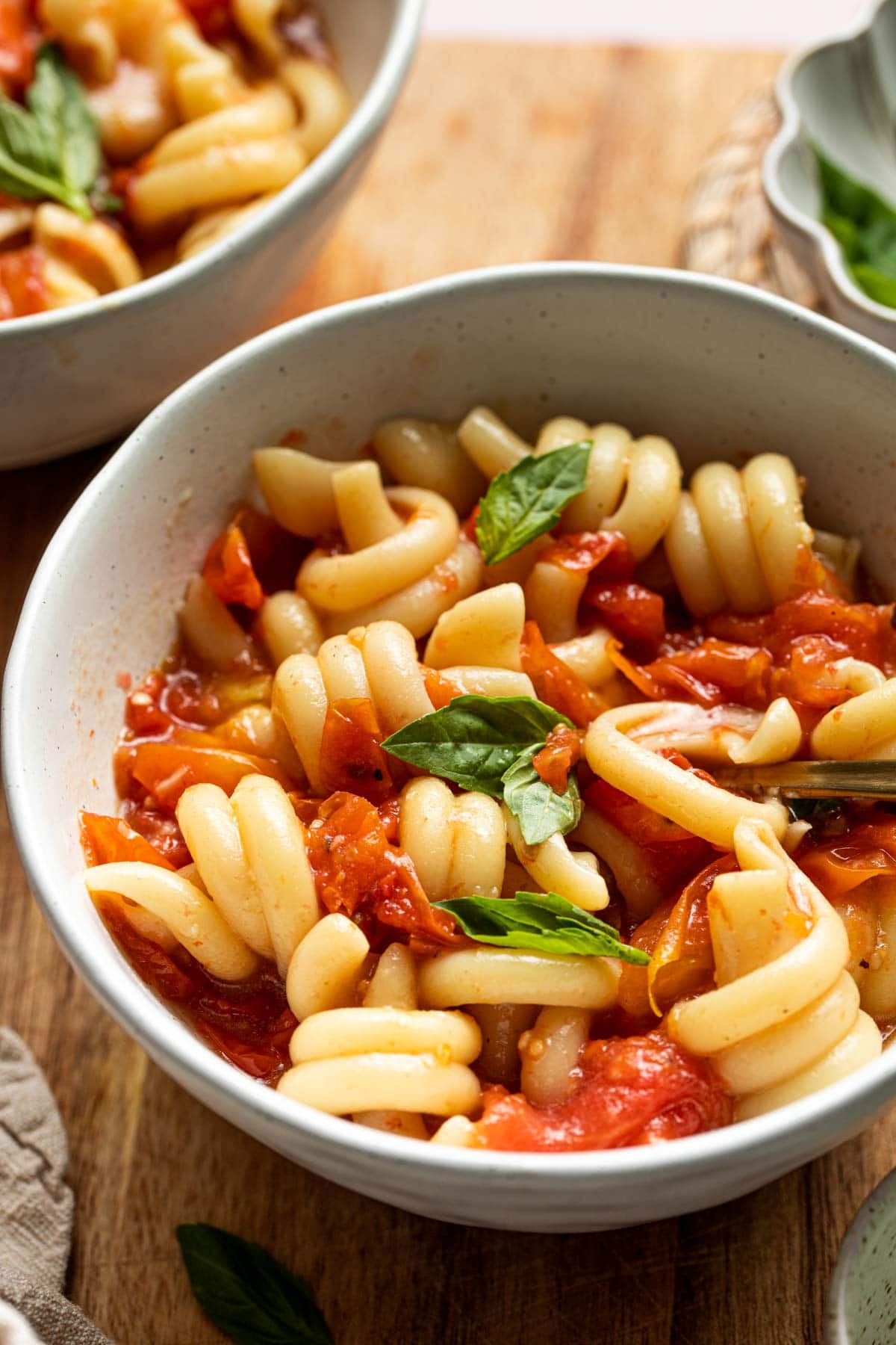 A side view of a bowl of tomato pasta with basil.