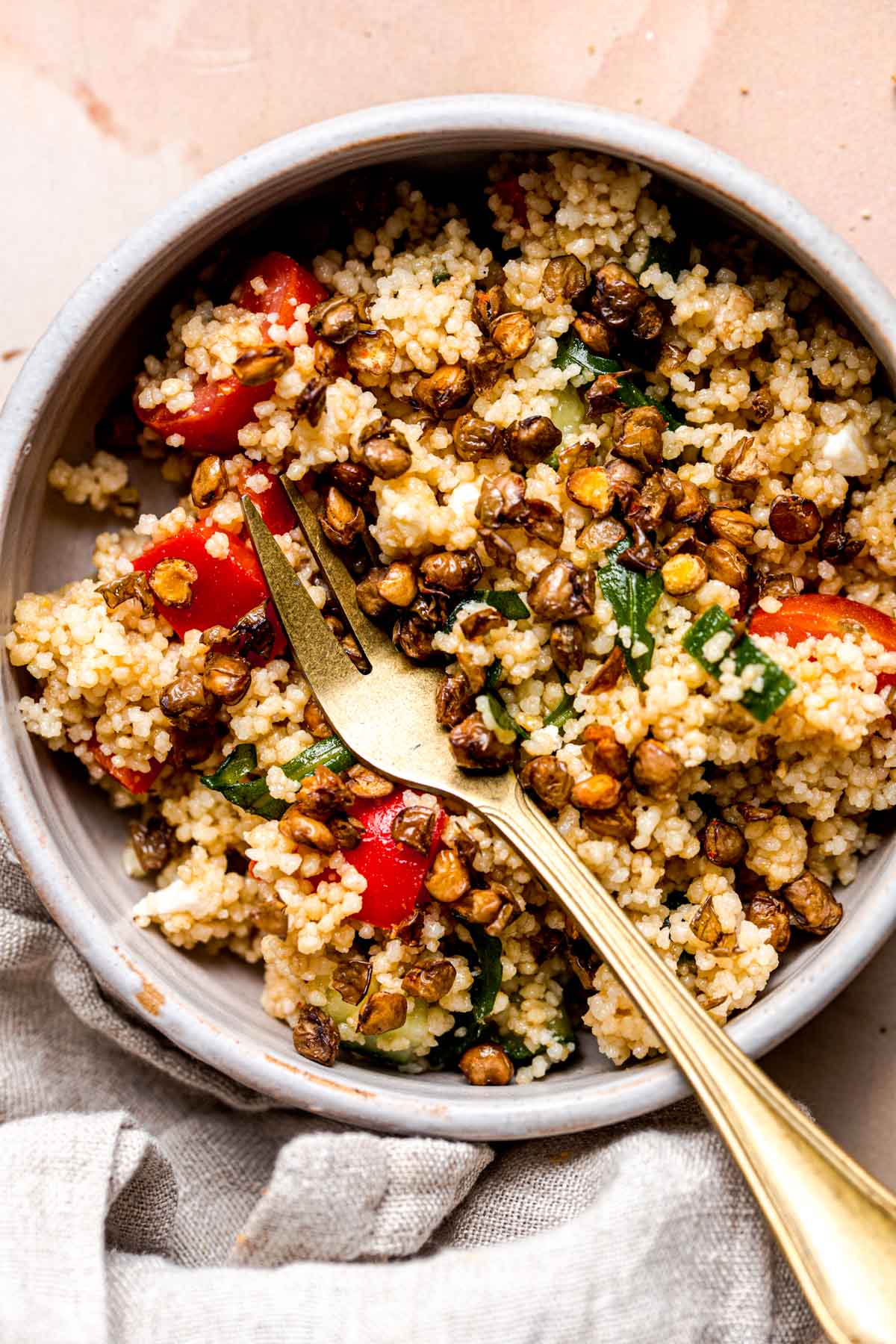 A bowl of vegetable couscous salad with a fork in the middle.