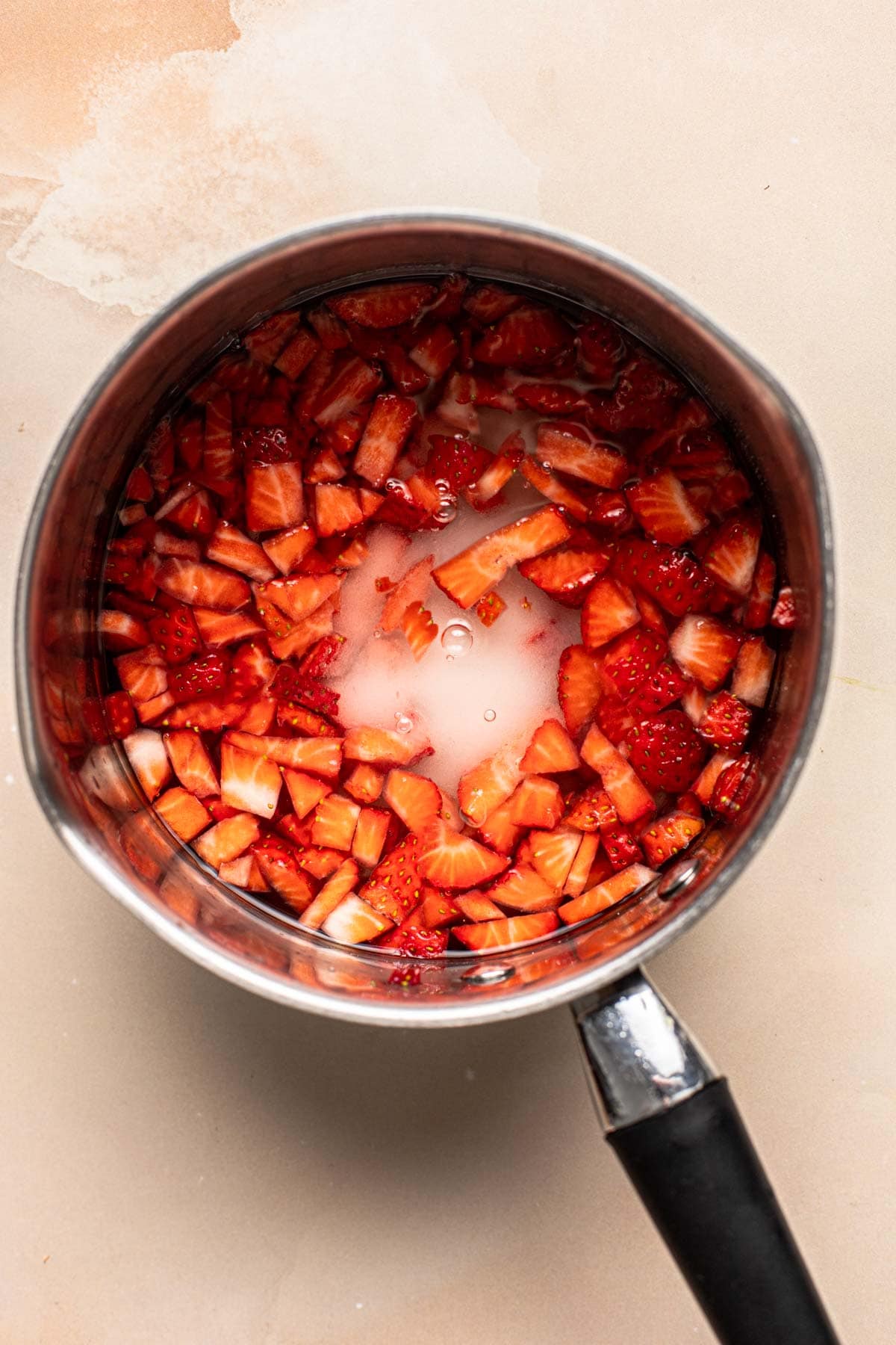 A small pan filled with sugar, water, and sliced strawberries.