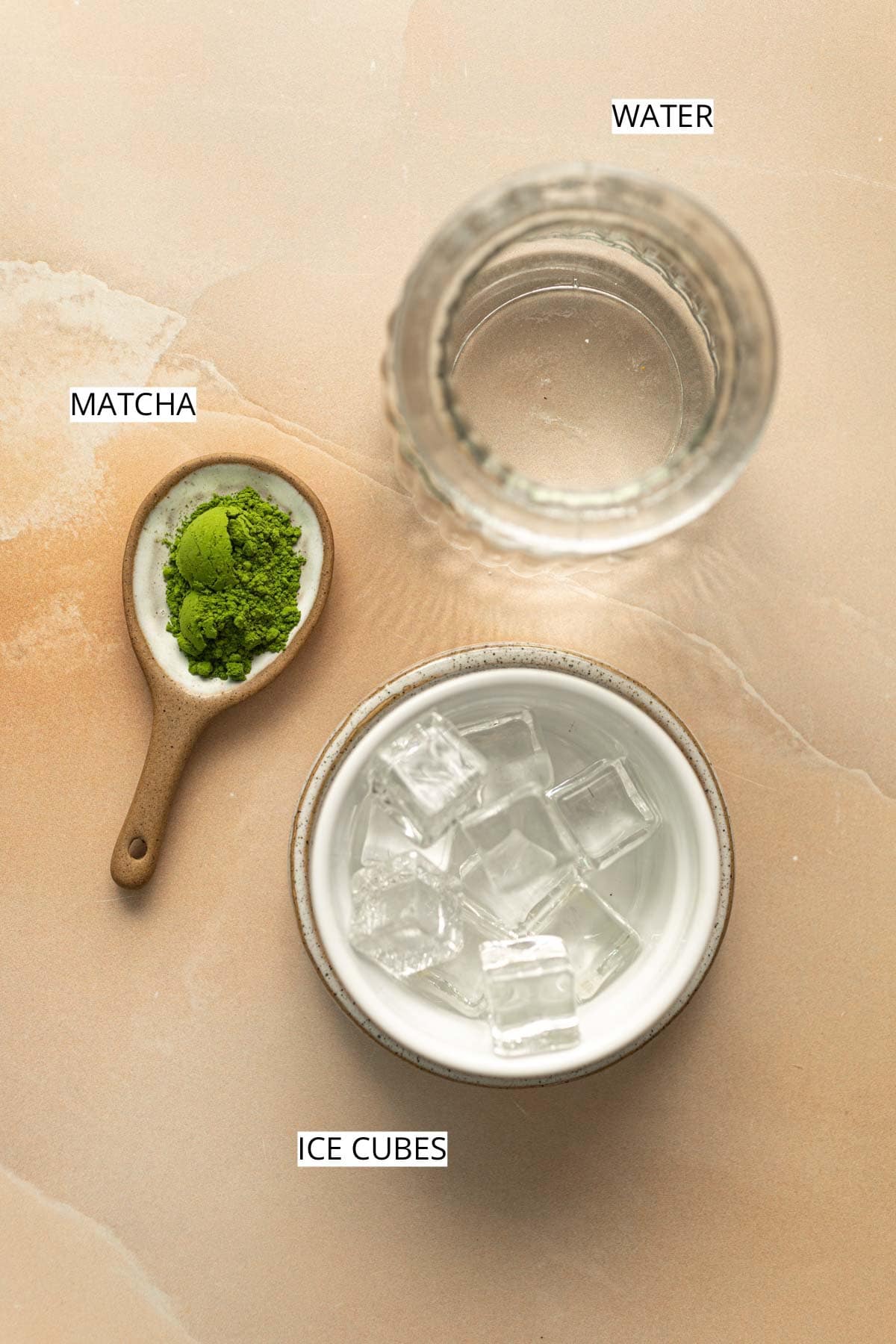 Water, matcha and ice cubes laid out on a flat surface.