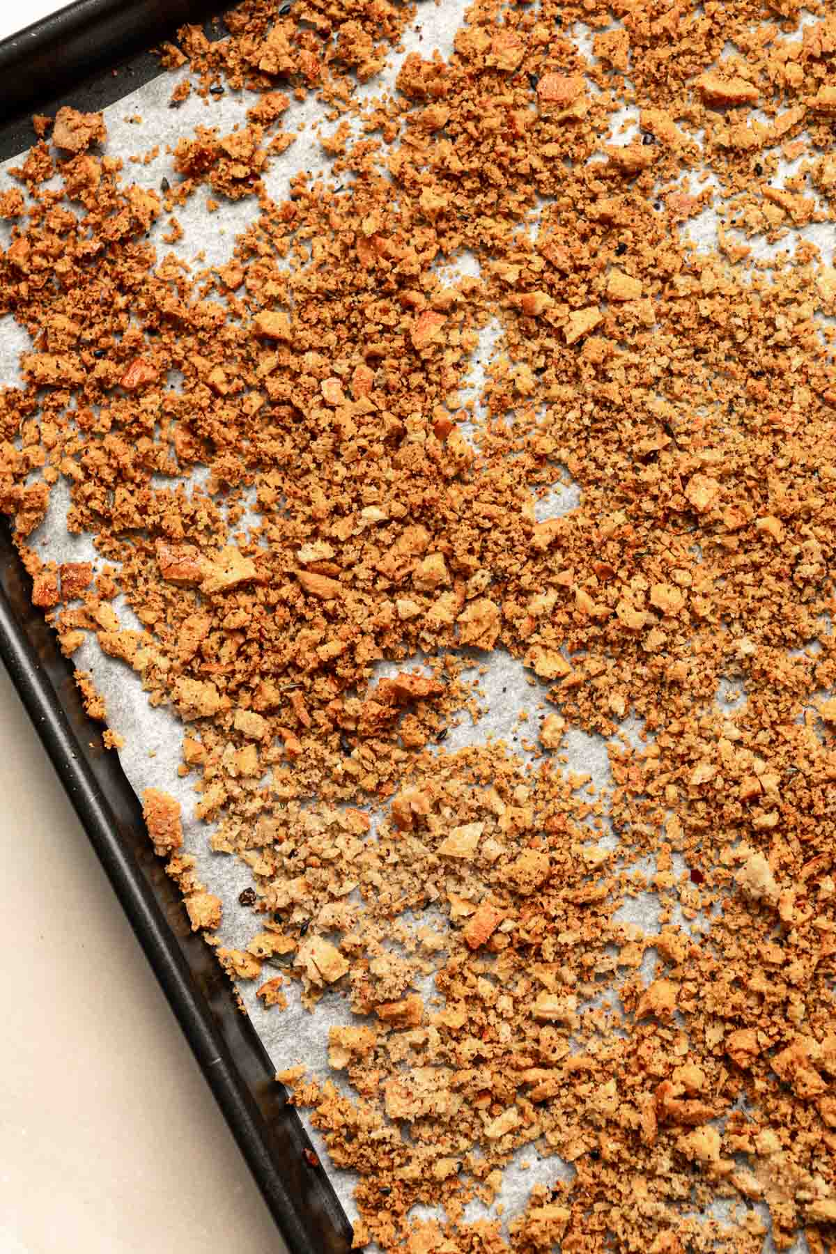 Breadcrumbs laid out on a lined baking sheet after baking in the oven.