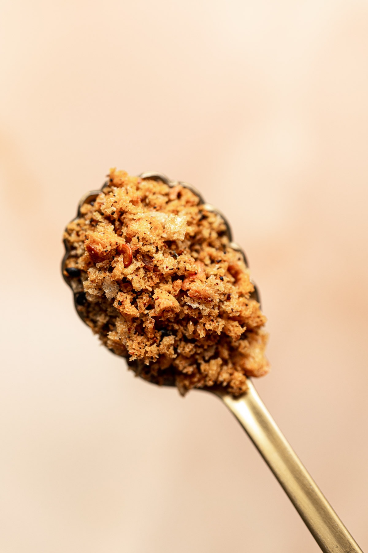 A gold spoon filled with breadcrumbs viewed from a close-up angle.