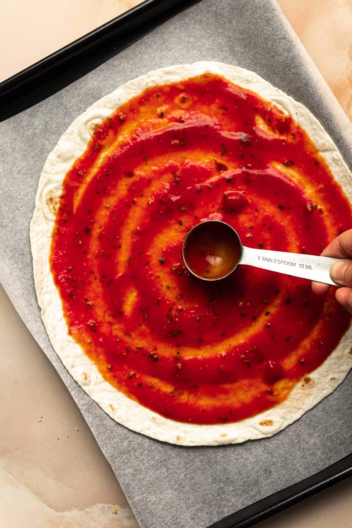 Tomato sauce being spread out on a tortilla pizza.