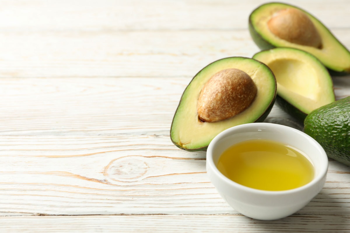 Ripe fresh avocado and oil on white wooden background, close up.