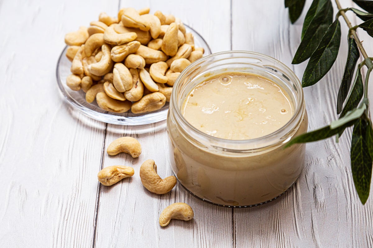 Cashews and cashew butter on a white wooden surface.
