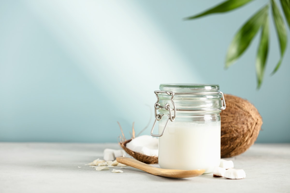 Coconut oil in a jar with fresh coconut and tropical leaves.