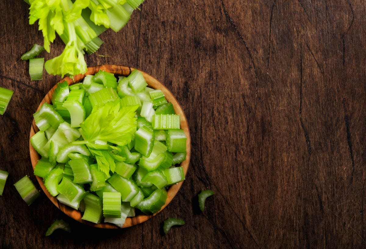 Green celery chopped pieces in bowl, wooden table, top view, copy space