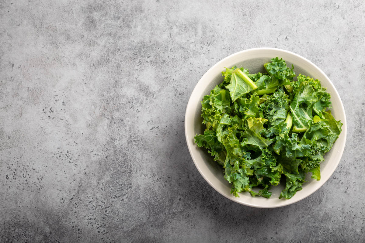 Bowl of fresh green chopped kale on gray rustic stone background, top view, close-up, copy space.