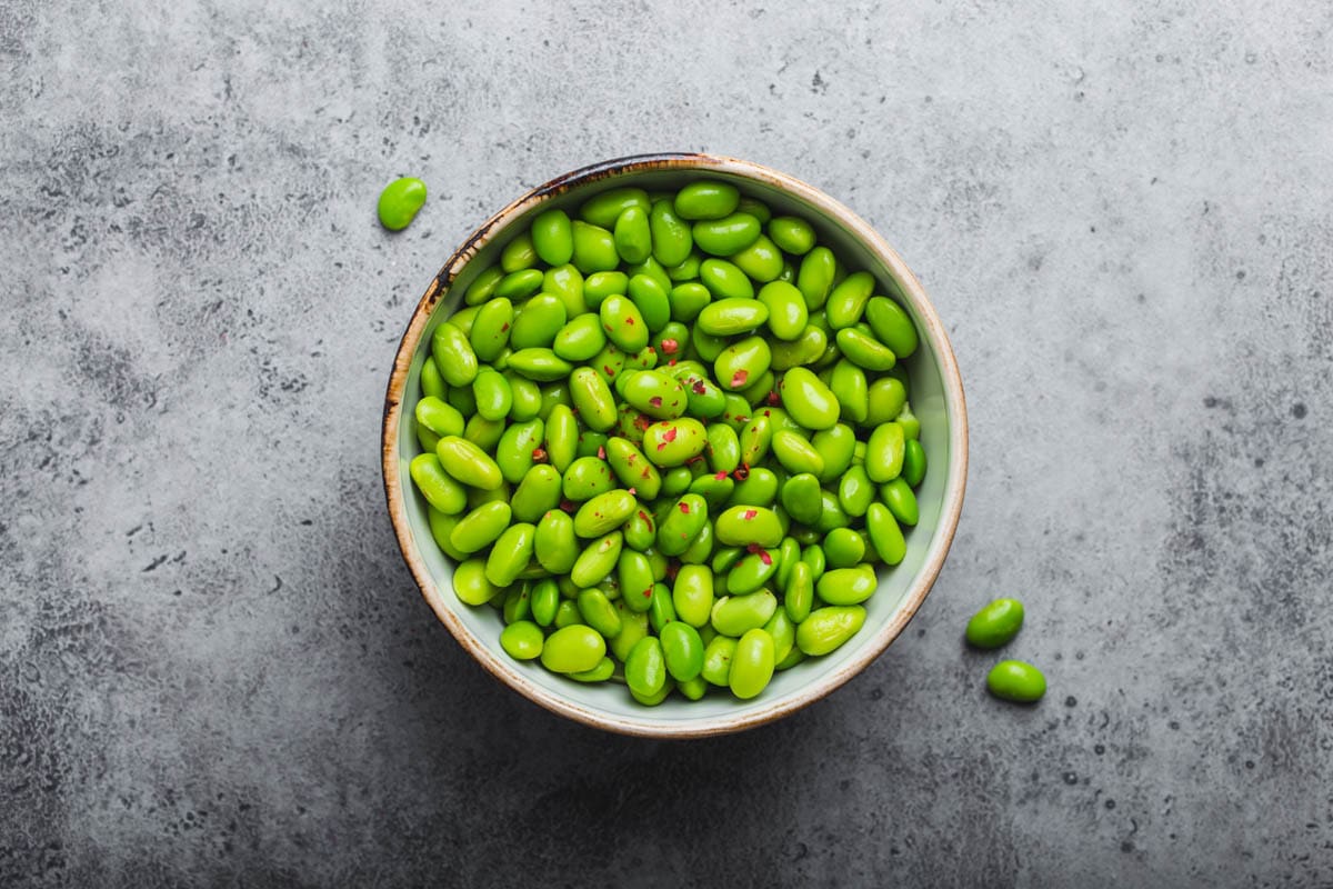 Fresh ripe green edamame beans without pods in bowl on gray stone background.