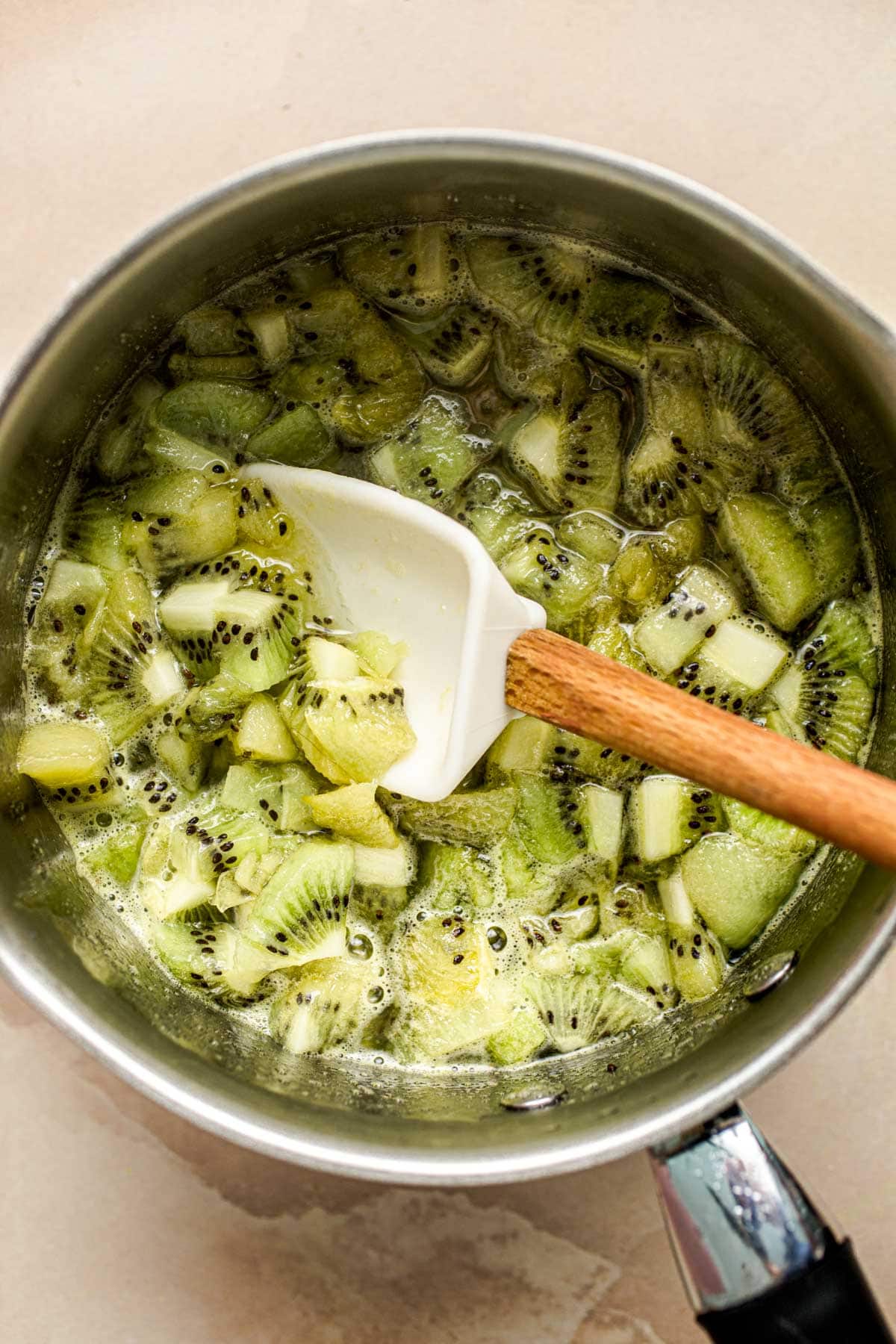 A small saucepan filled with kiwi chunks and a spatula in the middle.