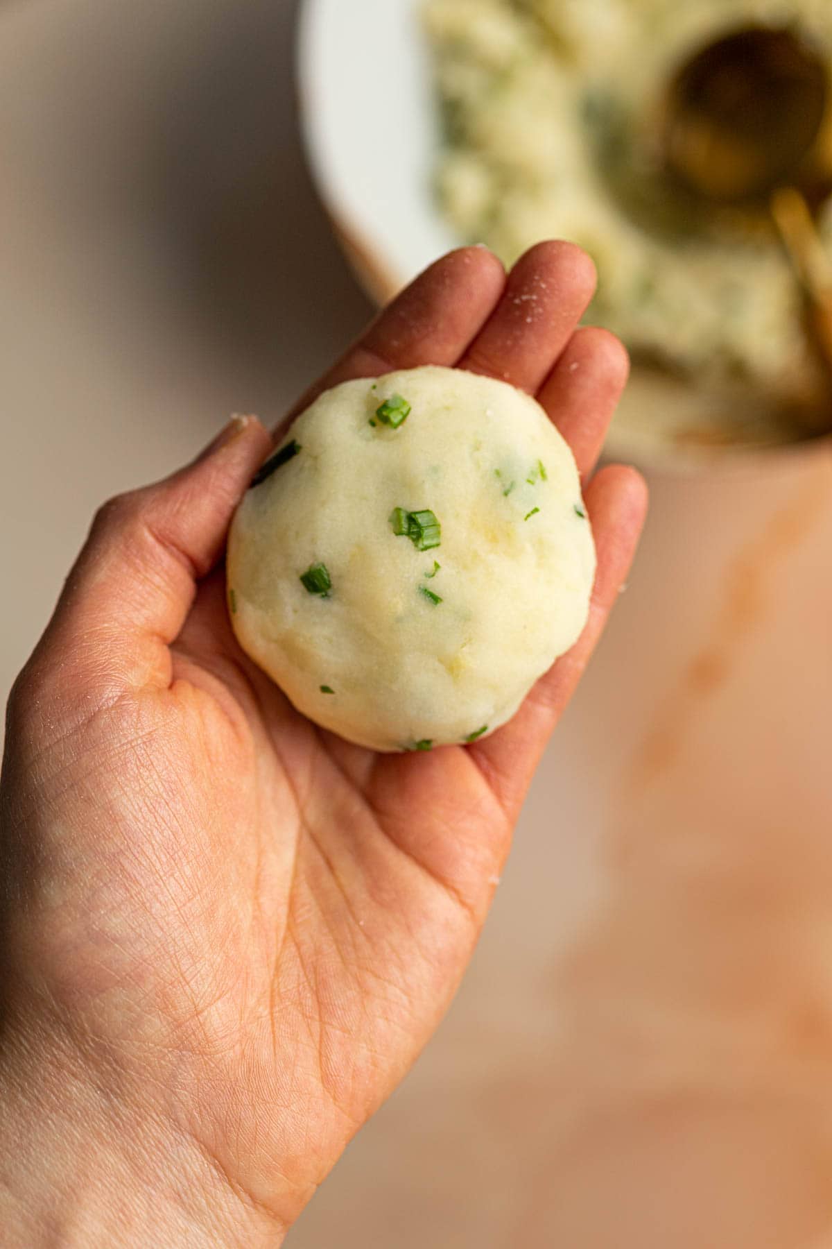A hand holding out potato chive mochi disc. 