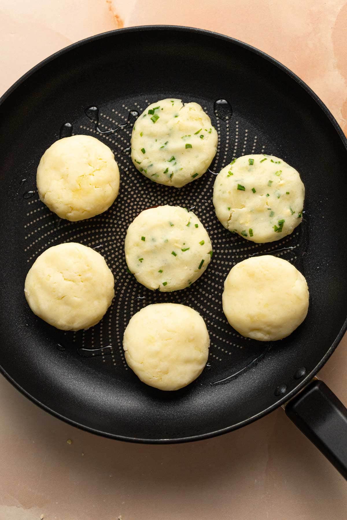 Seven potato mochi in a frying pan.