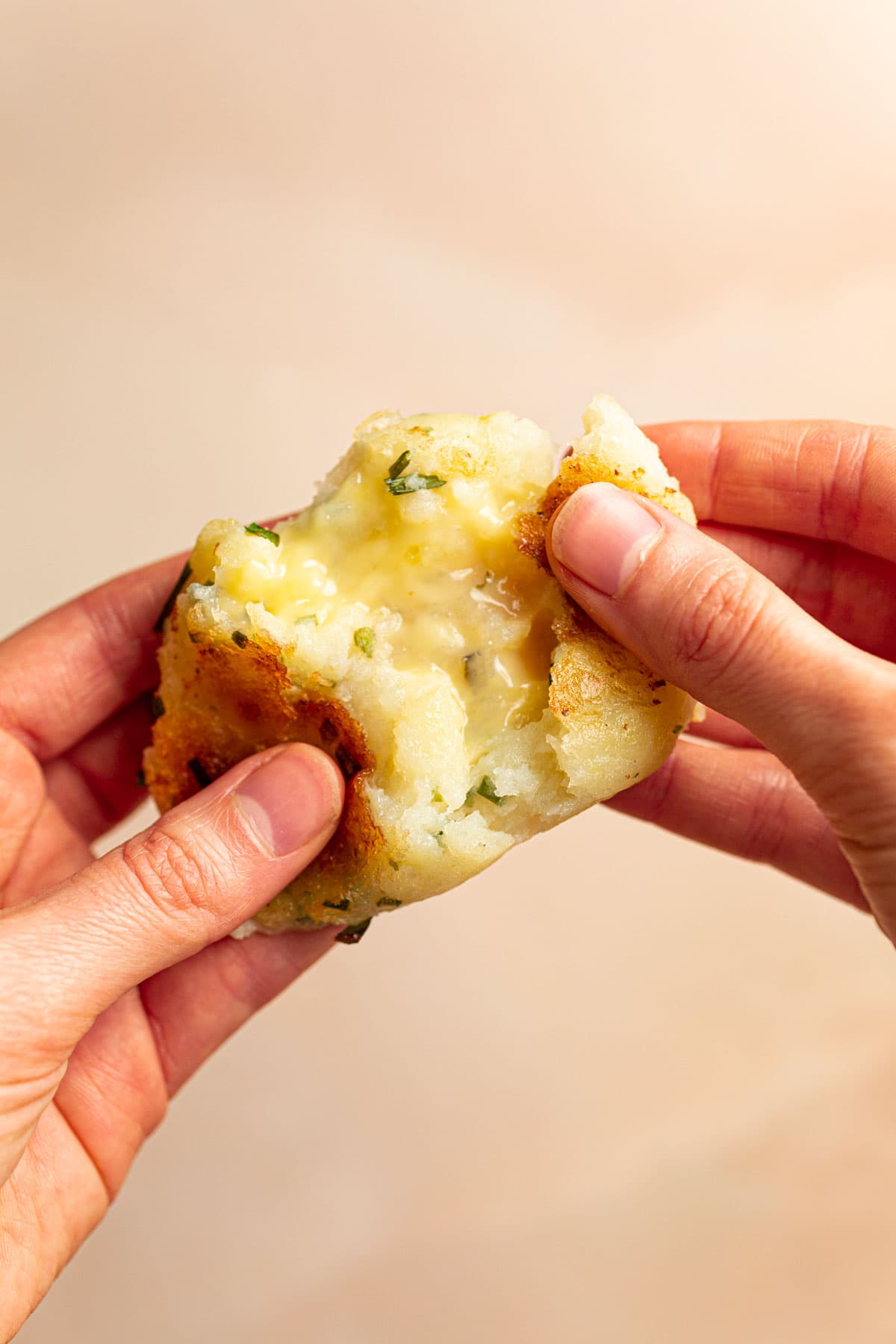 Two hands pulling apart a potato mochi stuffed with cheese.