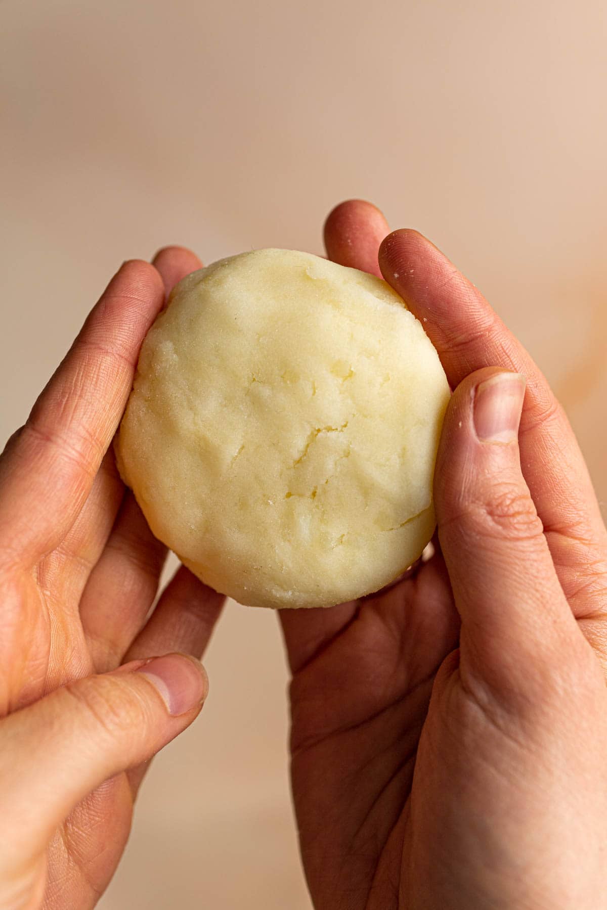 Two hands shaping a potato mochi into a disc.