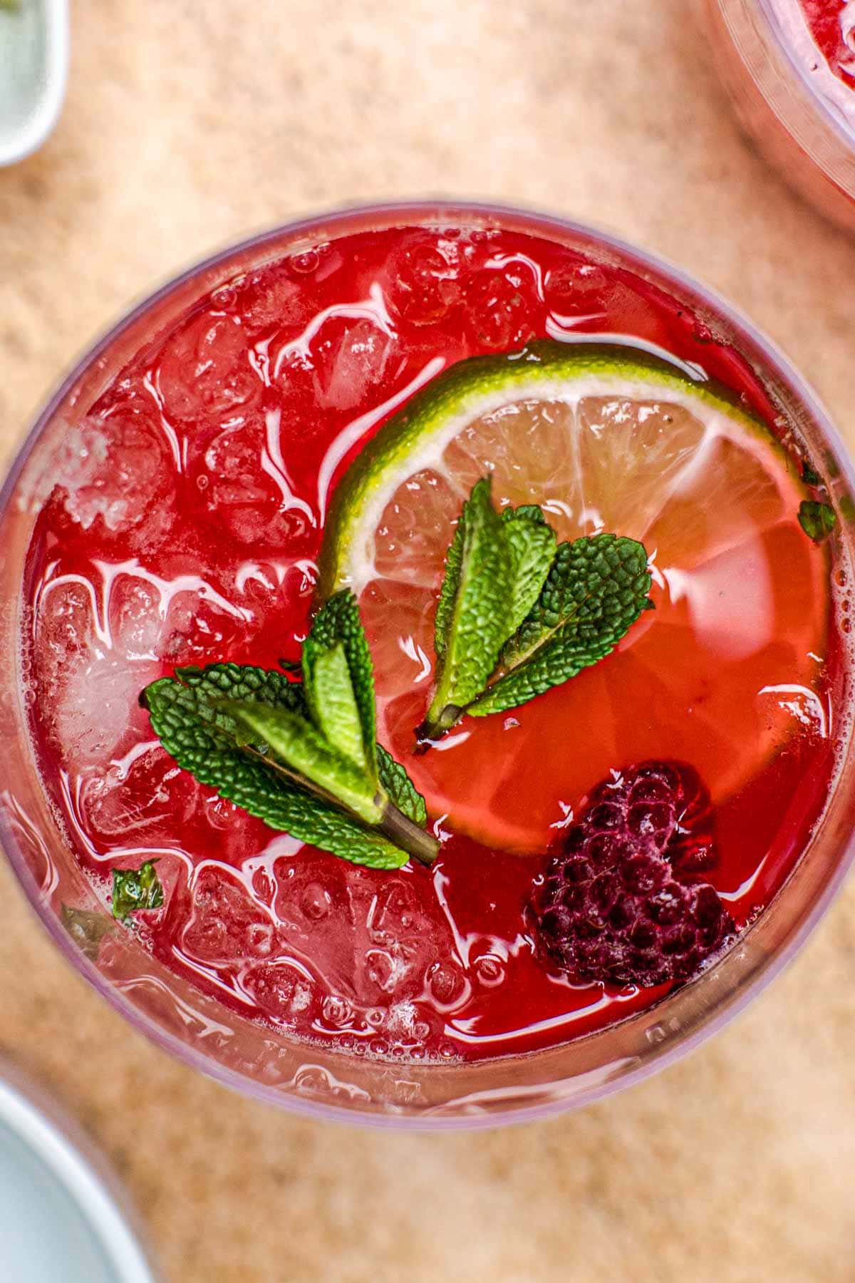A close-up overhead view of tequila smash topped off with mint leaves, lime and a raspberry.