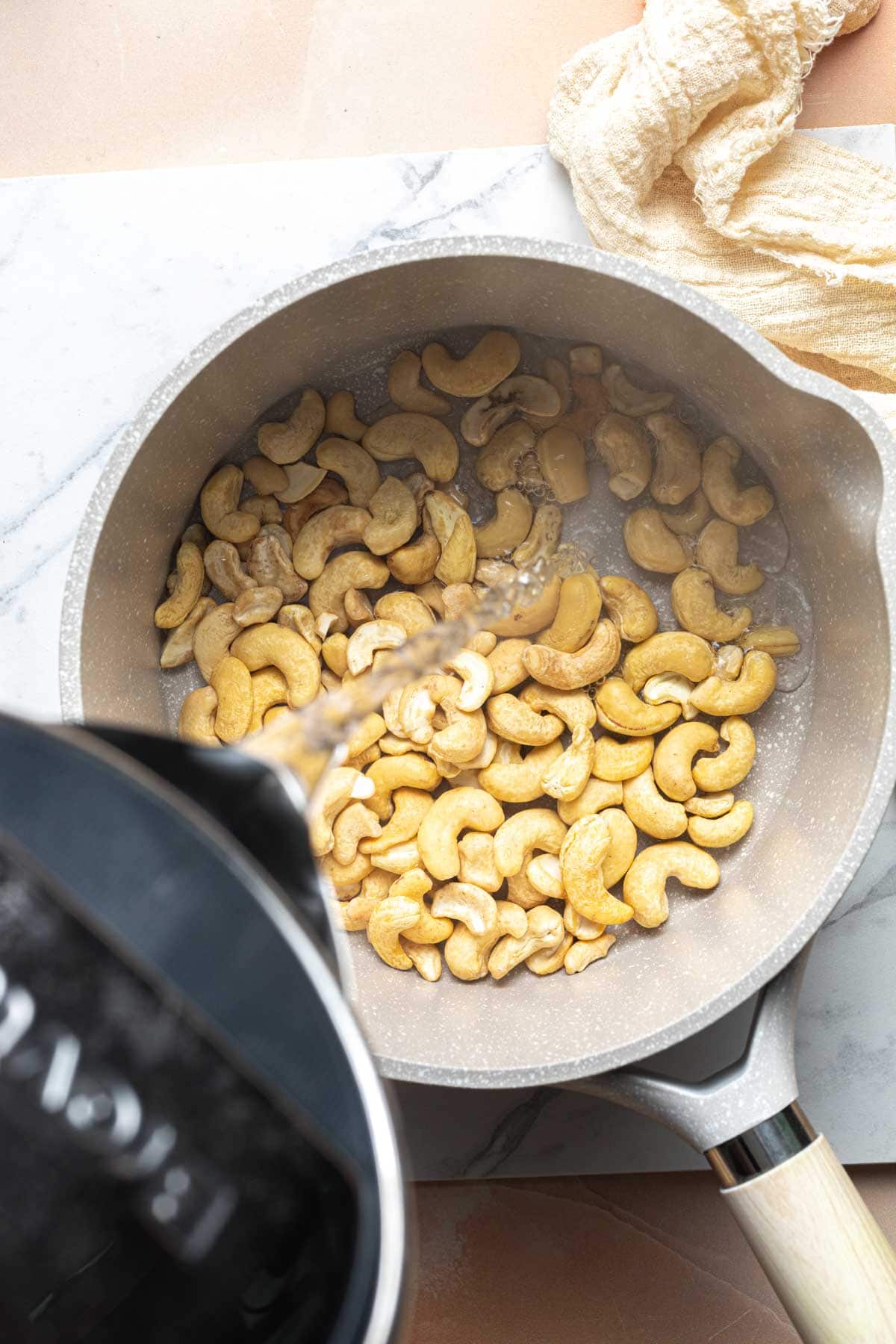 Boiling hot water being poured into a pan filled with cashews.