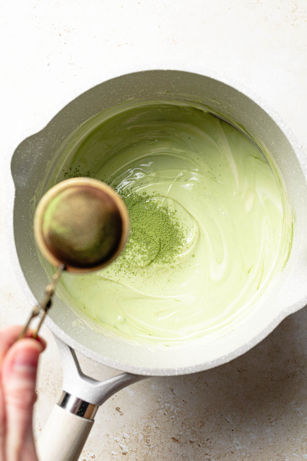 Matcha being sifted into a saucepan of melted white chocolate