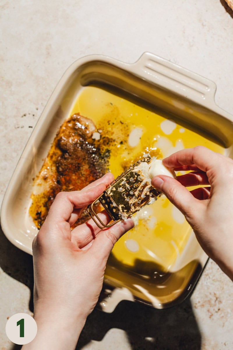 Garlic being grated into a shallow pan