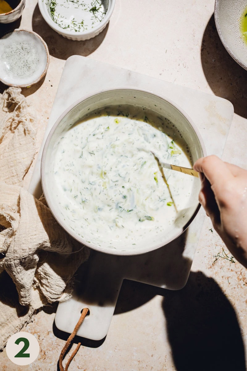 A hand mixing tzatziki ingredients