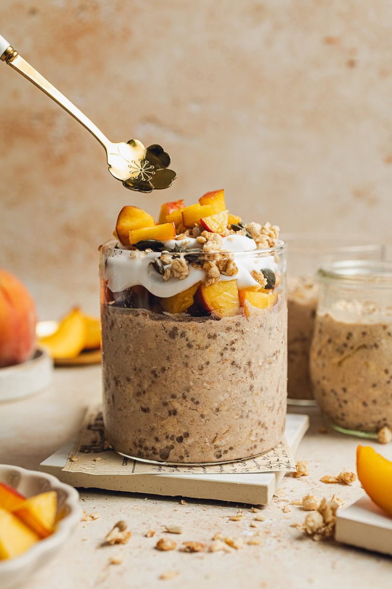 A spoon going towards the jar of overnight oats