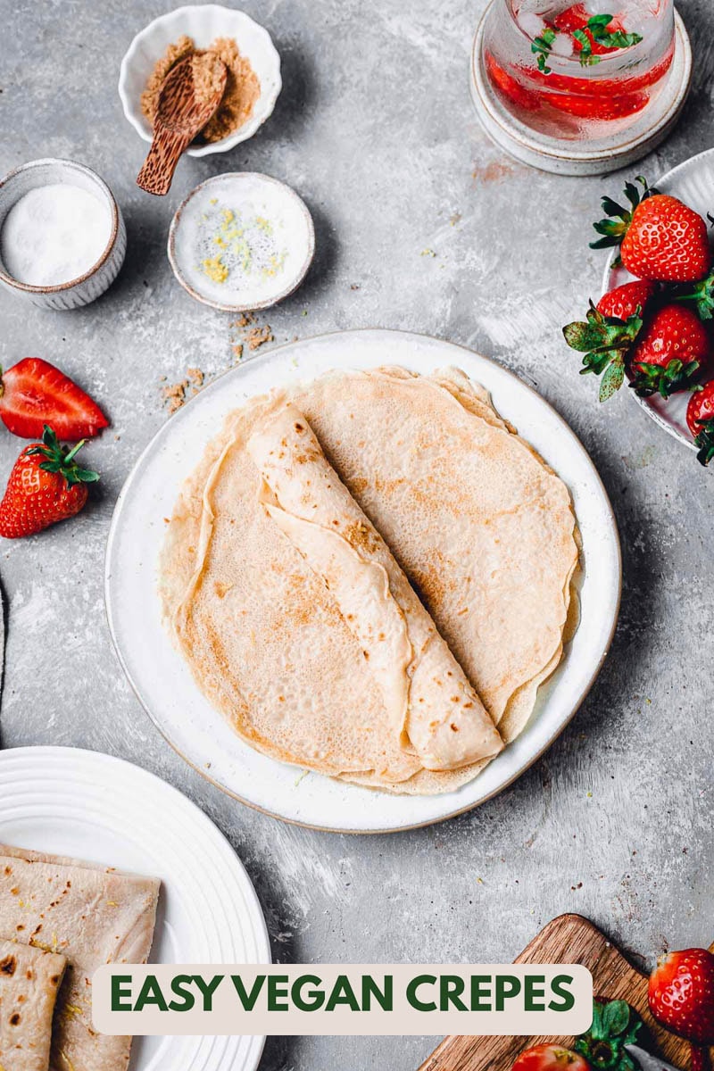 A plate of vegan crepes with strawberries scattered around the image