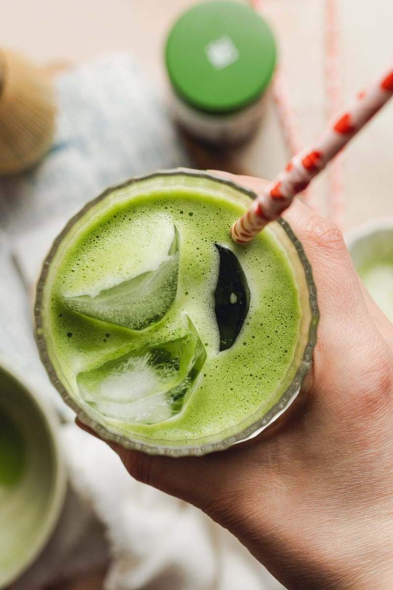 A person holding a glass of matcha americano