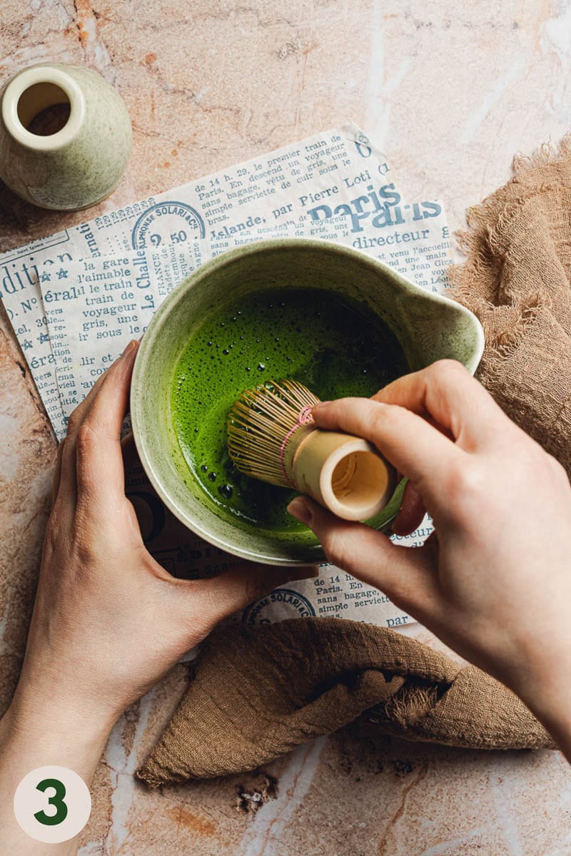 Hands using a bamboo whisk to whisk matcha